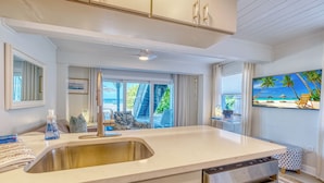 A modern kitchen with a stainless steel sink, a built-in oven, and a large window offering a view of a balcony with outdoor furniture.