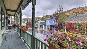 A covered porch with outdoor seating, a view of a street with colorful houses, and a hillside in the background. - Downtown Park City Vacation Rental, Near Ski Lift! (Park City)