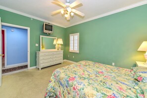 Une chambre à coucher comprenant un lit, une commode, un ventilateur de plafond, une télévision et une fenêtre avec des volets.