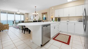A modern kitchen with white cabinets, a large island with a dishwasher, and a view to the outside.