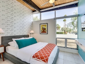 A bedroom with a bed, a wall of repeated text, a poster, and a view of the outside.