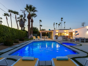 A swimming pool with lounge chairs, a barbecue area, and a building with a sign reading 'Palm Springs.'