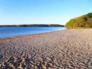 A sandy beach with a clear blue lake and a forested hill in the background. - Whip-o-Will Woods: Dog-Friendly Cape Cottage (Harwich)