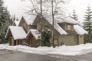 A cabin with a steeply pitched roof and snow-covered eaves, surrounded by snow-laden trees.