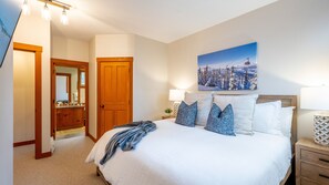 A bedroom with a large bed, a nightstand, a wall-mounted painting, and a wooden door.