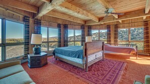 Quarto com uma cama grande, teto de madeira e vista da paisagem por grandes janelas.