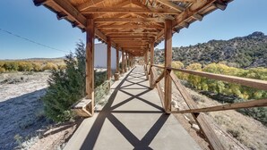 Uma ponte para pedestres de madeira com passarela de concreto, cercada por vegetação seca e um cenário montanhoso.