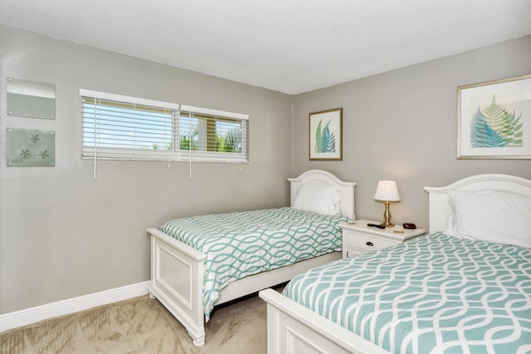 A bedroom with two beds, a window with blinds, a bedside table with a lamp, and framed artwork on the walls. - Condo# 319 Located across the street from Siesta Key Beach, Gulf and Pool View Condo!! (Sarasota)