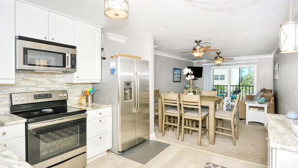 A modern kitchen with stainless steel appliances, a dining area with wooden chairs, and a ceiling fan. - Condo# 319 Located across the street from Siesta Key Beach, Gulf and Pool View Condo!! (Sarasota)
