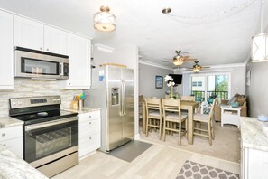 A modern kitchen with stainless steel appliances, a dining area with wooden chairs, and a ceiling fan. - Condo# 319 Located across the street from Siesta Key Beach, Gulf and Pool View Condo!! (Sarasota)