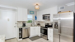 A modern kitchen with white cabinets, stainless steel appliances, and a decorative seahorse wall hanging. - Condo# 319 Located across the street from Siesta Key Beach, Gulf and Pool View Condo!! (Sarasota)