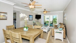 A dining area with a wooden table and chairs, two ceiling fans, and a view to an outdoor patio. - Condo# 319 Located across the street from Siesta Key Beach, Gulf and Pool View Condo!! (Sarasota)