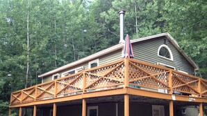 A wooden deck with a covered area, a chimney, and a house with a window and door.