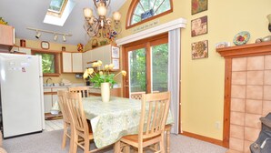 A kitchen with wooden cabinets, a refrigerator, a dining table with chairs, and a window with a view of trees.