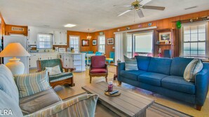 A cozy living room with a blue sofa, a wooden coffee table, and a dining area with a table and chairs. - The Choice: Oceanfront Comfort in Surf City (Surf City)