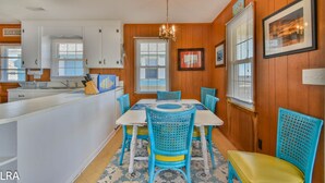A kitchen with wooden paneling, a dining area with blue chairs, a chandelier, and a framed picture on the wall. - The Choice: Oceanfront Comfort in Surf City (Surf City)