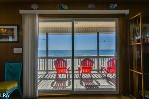 Une chambre avec vue sur l’océan, dotée d’une porte-fenêtre coulissante, de deux fauteuils Adirondack rouges et d’une terrasse en bois.