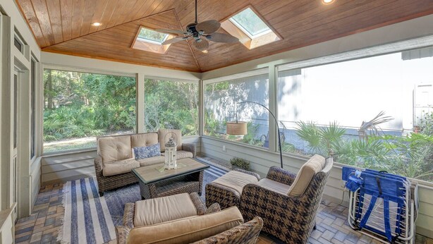 A sunroom with a wooden ceiling, large windows, and wicker furniture.