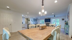 A spacious dining area with a wooden table and chairs, a chandelier, and a view of the kitchen and living area.
