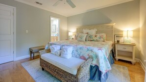 A bedroom with a bed, a bench, two bedside tables, a ceiling fan, and a door.