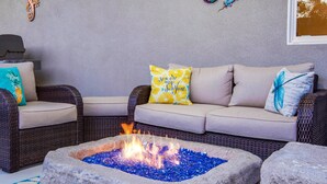 A cozy seating area with a stone fire pit, wicker furniture, and decorative pillows. - Sun Haven Escape – Designer Palm Springs Retreat (Palm Springs)