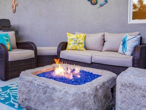 A cozy seating area with a stone fire pit, wicker furniture, and decorative pillows.