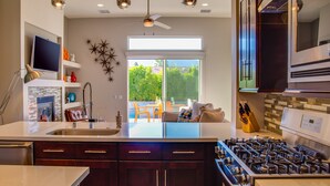 A modern kitchen with dark wood cabinets, a stainless steel range, and a large window overlooking a patio. - Sun Haven Escape – Designer Palm Springs Retreat (Palm Springs)