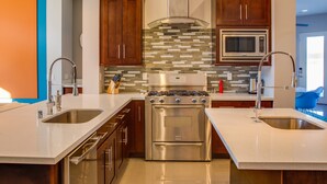 A modern kitchen with stainless steel appliances, wooden cabinets, and a tiled backsplash. - Sun Haven Escape – Designer Palm Springs Retreat (Palm Springs)