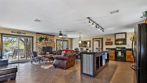 A spacious living area with a fireplace, leather sofa, and a dining table. - 3 Bedroom/3 Bath home overlooking 2 Creeks with Hot Tub and Fire Pit! (Wimberley)