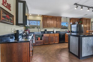 A modern kitchen with wooden cabinets, a black countertop, and a built-in island. - 3 Bedroom/3 Bath home overlooking 2 Creeks with Hot Tub and Fire Pit! (Wimberley)