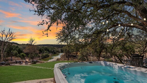 A hot tub with a view of a river and trees at sunset. - 3 Bedroom/3 Bath home overlooking 2 Creeks with Hot Tub and Fire Pit! (Wimberley)