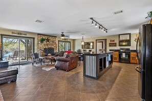 A spacious living area with a fireplace, leather sofa, and a dining table. - 3 Bedroom/3 Bath home overlooking 2 Creeks with Hot Tub and Fire Pit! (Wimberley)