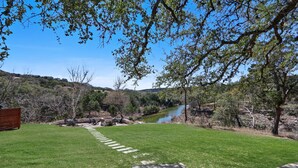 A grassy outdoor area with a stone pathway leading to a seating area with benches and a table. - 3 Bedroom/3 Bath home overlooking 2 Creeks with Hot Tub and Fire Pit! (Wimberley)
