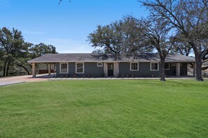 A single-story house with a flat roof, a brick foundation, and a covered porch. - 3 Bedroom/3 Bath home overlooking 2 Creeks with Hot Tub and Fire Pit! (Wimberley)