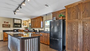 A modern kitchen with wooden cabinets, a black refrigerator, and a central island. - 3 Bedroom/3 Bath home overlooking 2 Creeks with Hot Tub and Fire Pit! (Wimberley)