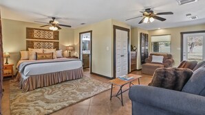 A bedroom with a bed, bedside tables, a nightstand, a ceiling fan, a door, and a view of the outdoors. - 3 Bedroom/3 Bath home overlooking 2 Creeks with Hot Tub and Fire Pit! (Wimberley)