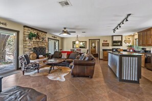 A spacious living area with a fireplace, leather sofas, and a stone accent wall. - 3 Bedroom/3 Bath home overlooking 2 Creeks with Hot Tub and Fire Pit! (Wimberley)