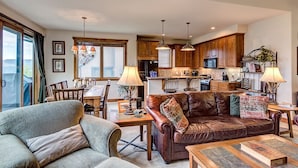 A spacious living room with a leather sofa, a dining area with a wooden table, and a kitchen with wooden cabinets and pendant lighting. - Private Hot Tub, Ski-in/ski-out! (Breckenridge)