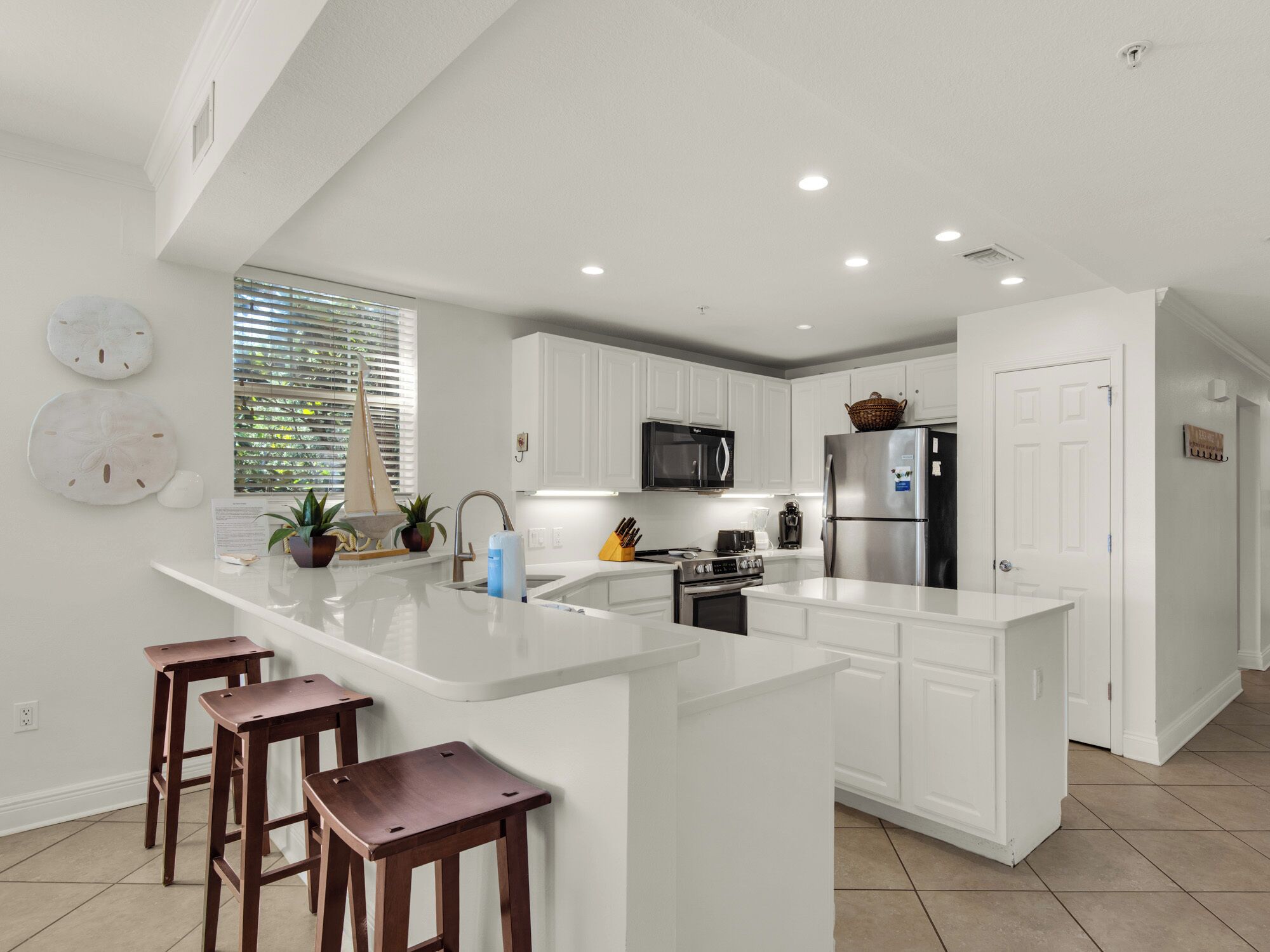 Una cocina moderna con armarios blancos, una isla central con taburetes, microondas, estufa y refrigerador.