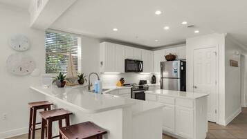 Una cocina moderna con armarios blancos, una isla central con taburetes, microondas, estufa y refrigerador.