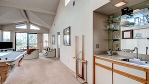 Amplia sala de estar con mesa de billar, sofá y cocina equipada con lavamanos y cristalería.