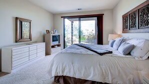 Un dormitorio con una cama grande, un aparador, un televisor y una ventana con vistas a zonas verdes.