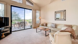 Amplia sala de estar con un gran ventanal corredizo que da a un patio exterior, un sofá, una mesa de centro y un televisor de pantalla plana.