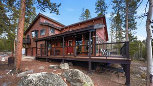 Une cabane à deux étages avec une terrasse, entourée d’arbres et de rochers.