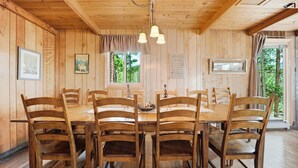 Une cabane en bois avec une table à manger entourée de chaises, un lustre et une fenêtre donnant sur les arbres.