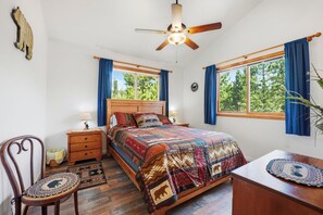 A bedroom with a bed, a wooden nightstand, a chair, a desk, a ceiling fan, and two windows with curtains. - Large Home on 1 Acre: 2 Mi to Grand Lake Village (Grand Lake)