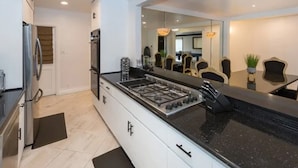 A modern kitchen with white cabinets, a black countertop, and a stainless steel range hood. - Luxurious 3-Bedroom Westwood Gem  (Los Angeles)