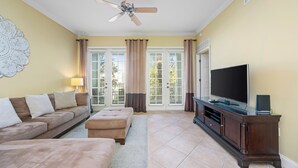 A living room with a sofa, ottoman, TV, and entertainment unit. - Beautiful Luxury Condo with Upgraded Kitchen! Only Minutes to Disney (Kissimmee)