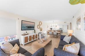 A modern living room with a sofa set, a coffee table, and a TV. There is a dining area with a table and chairs.