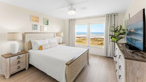 Un dormitorio con cama, mesitas de noche, televisor y vista a la playa.